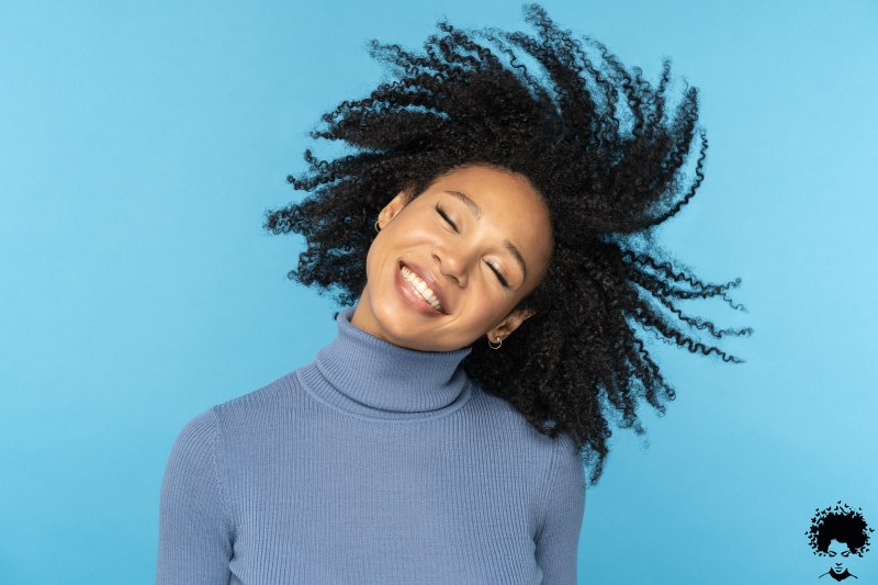 happy afro woman smiling has good mood dancing with her black curly hair flying isolated on blue 1 1